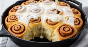 cast iron skillet filled with warm sourdough discard cinnamon rolls and frosting