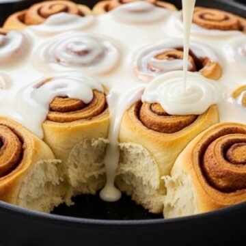 cast iron skillet filled with warm sourdough discard cinnamon rolls and frosting