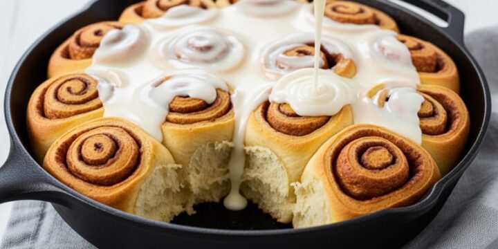 cast iron skillet filled with warm sourdough discard cinnamon rolls and frosting